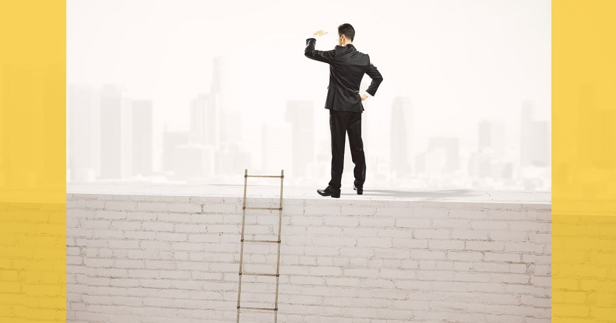 塀の上にのぼって遠くを眺めるビジネスパーソン