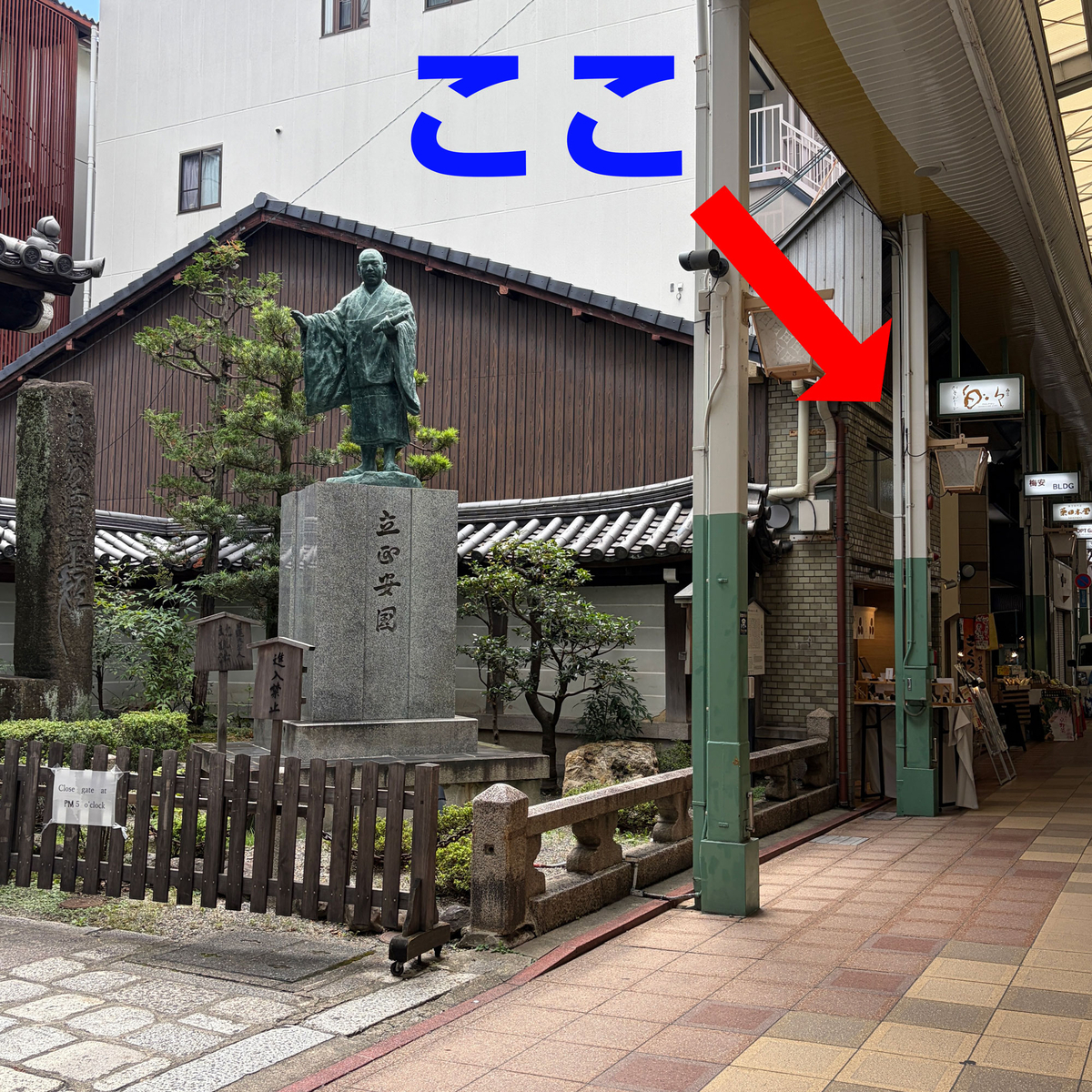 銅像のそばに「ここ」の文字と矢印で店の場所を示した写真