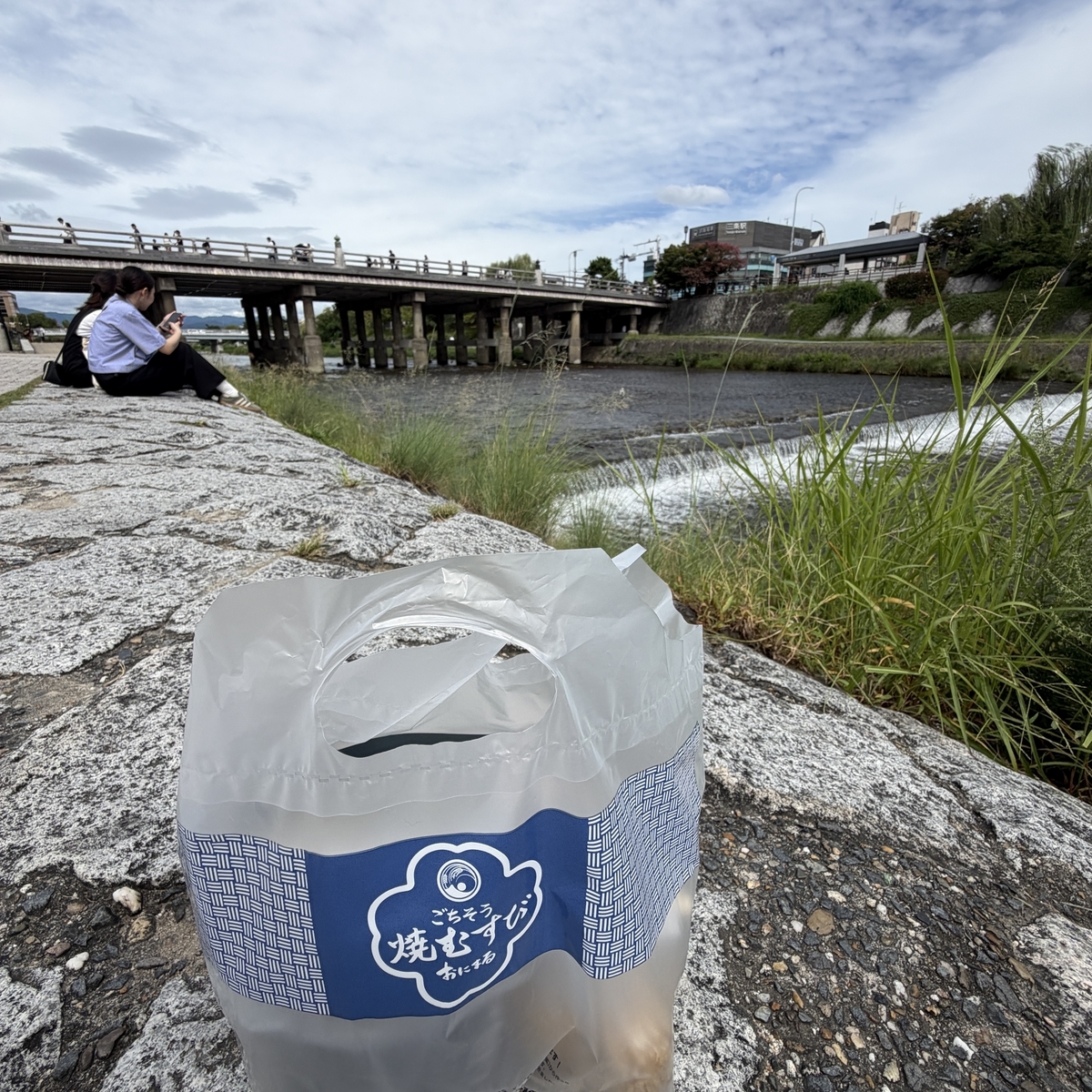 おにまるのロゴ入りの袋と鴨川・三条大橋