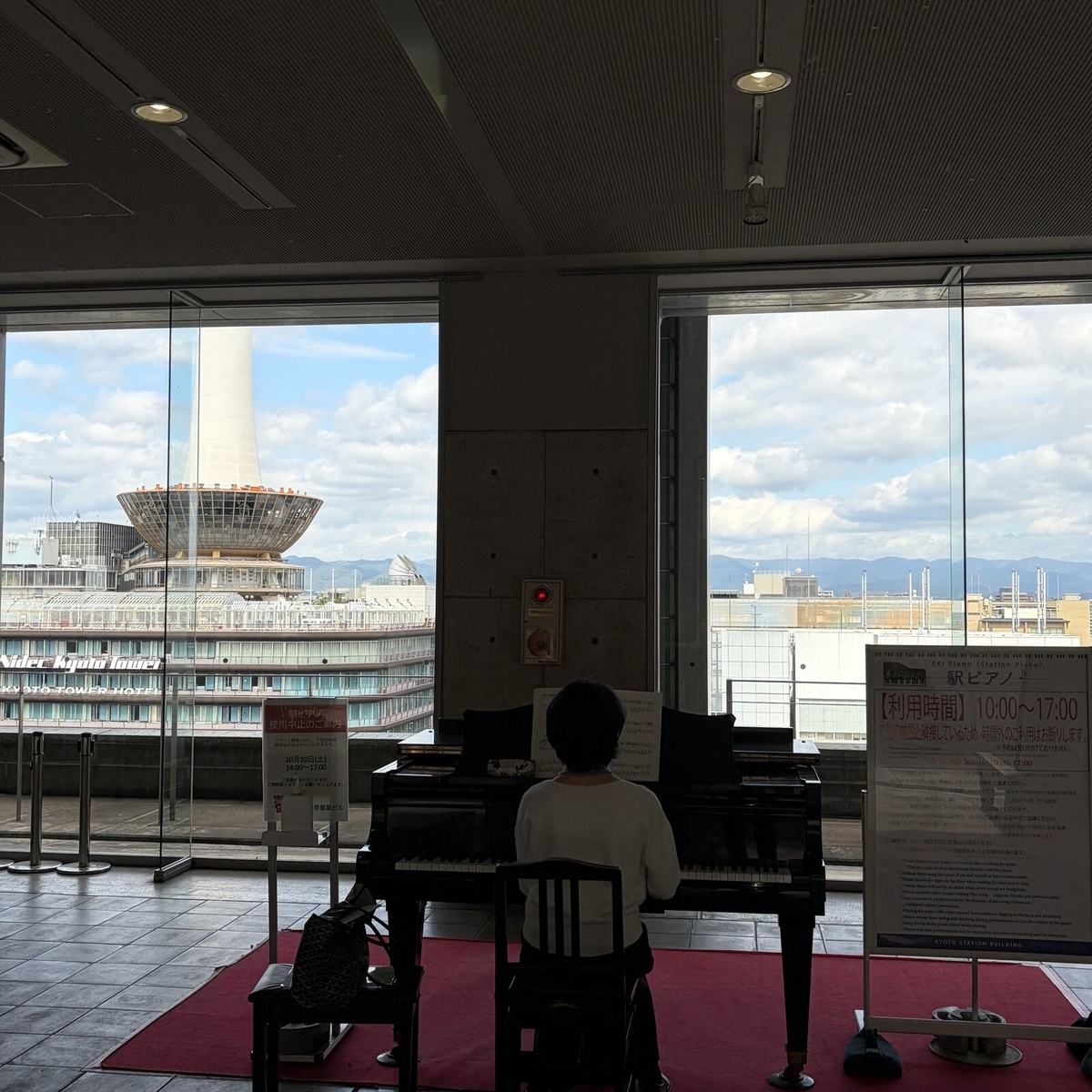 京都タワーが見える窓辺に置かれた駅ピアノと演奏する人