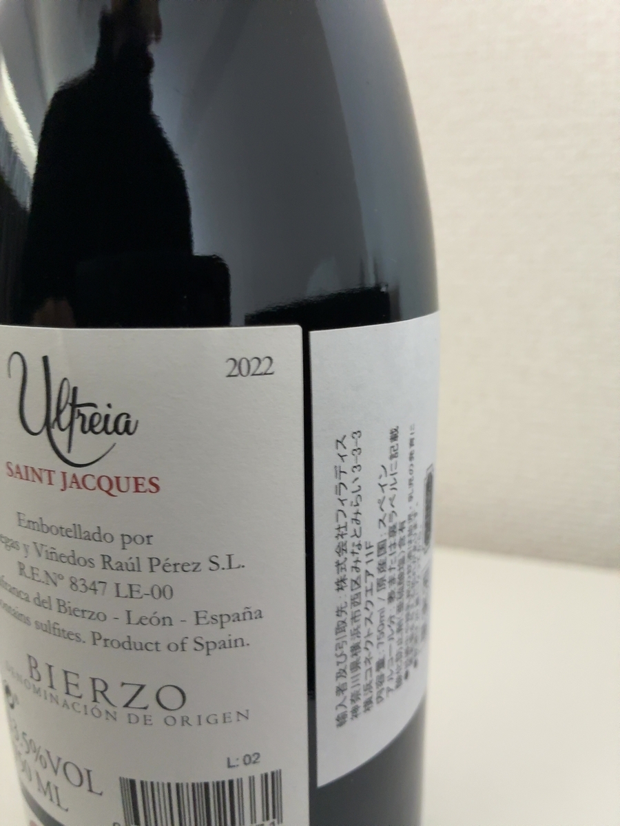 ボトルの左側には「Ultreia SAINT JACQUES」という文字が書かれており、その右隣には「2022」という数字が見えます。その下には「Embotellado por Bodegas y Viñedos Raúl Pérez S.L.」とあり、さらに「R.E.N° 8347 LE-00」と続いています。その下には「Valtuille de Abajo, Carracedelo, Ponferrada, El Bierzo - León - España」と書かれており、その下には「Contains sulfites. Product of Spain.」と記載されています。さらにその下には「BIERZO」という大きな文字と「DENOMINACIÓN DE ORIGEN」という文字が確認できます。 ボトルの右側には、輸入者および引取先として「株式会社フィラディス」とあり、その住所が「神奈川県横浜市西区みなとみらい3-3-3 横浜コネクトスクエア11F」と記されています。内容量は「750ml」、原産国は「スペイン」と書かれています。アルコール分については「表または裏ラベルに記載」とあり、酸化防止剤として「亜硫酸塩」が含まれていることが示されています。その下には「妊娠中や授乳期の飲酒は、胎児・乳児の発育に悪影響を与えるおそれがあります。」という注意書きが一部見えます。 ボトルの下部にはバーコードの一部と「L: 02」という文字が確認できます。ボトル自体は濃い色をしており、光沢があります。