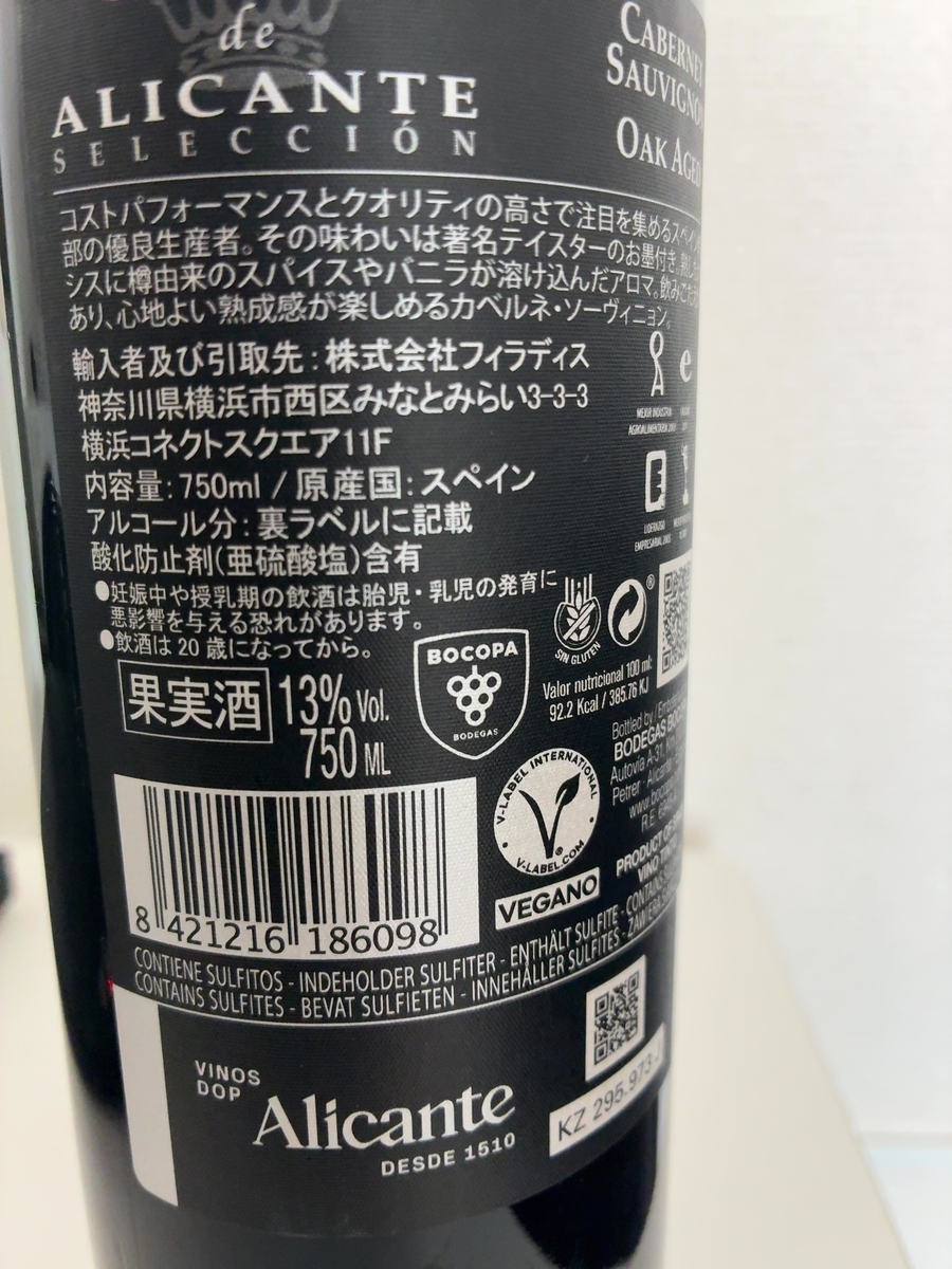 ラベルには「ALICANTE SELECCIÓN」と書かれており、これはスペインのワイン産地であるアリカンテのセレクションであることを示唆しています。また、「CABERNE SAUVIGNON OAK AGED」という文字も見え、カベルネ・ソーヴィニヨン種がオーク樽で熟成されたワインであることがわかります。 さらに、「コストパフォーマンスとクオリティの高さで注目を集めるスペイン部の優良生産者。その味わいは著名テイスターのお墨付き、シスに樽由来のスパイスやバニラが溶け込んだアロマ。飲みごたえあり、心地よい熟成感が楽しめるカベルネ・ソーヴィニョン。」という説明文があり、ワインの特徴が記されています。 輸入者および引取先は「株式会社フィラディス」、住所は「神奈川県横浜市西区みなとみらい3-3-3 横浜コネクトスクエア11F」と記載されています。内容量は750mlで、原産国はスペインです。アルコール分は裏ラベルに記載されており、酸化防止剤(亜硫酸塩)が含まれていることも明記されています。 「果実酒 13% Vol. 750 ML」という表示もあり、アルコール度数と容量が確認できます。バーコードの下には、「CONTAINS SULFITES - BEVAT SULFIETEN - INNEHÅLLER SULFITES - ZAINER」といった複数の言語で亜硫酸塩が含まれていることを示す表記が見られます。 「VEGANO」という文字と、ヴィーガン認証マークのようなものも確認できます。また、「BOCOPA BODEGAS」という文字も見えます。 ラベルの下部には、「VINOS DOP Alicante DESDE 1510」と書かれており、アリカンテの原産地呼称(DOP)ワインであることがわかります。