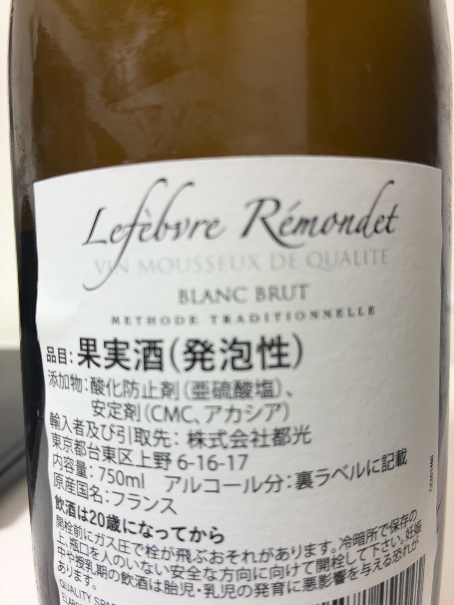 この画像には、Lefebvre Rémondetというブランド名の白ワインのボトルが写っています。 ボトルのラベルには、フランス語で「VIN MOUSSEUX DE QUALITE BLANC BRUT METHODE TRADITIONNELLE」と書かれており、これは「高品質の発泡性ワイン、ブリュット、伝統的な製法」という意味です。 日本語で書かれた部分には、「品目:果実酒(発泡性)」、「添加物:酸化防止剤(亜硫酸塩)、安定剤(CMC、アカシア)」と記載されています。また、「輸入者及び引取先:株式会社都光 東京都台東区上野6-16-17」という情報も見られます。 内容量は750mlで、アルコール分は裏ラベルに記載されているとのことです。原産国はフランスと明記されています。 さらに、「飲酒は20歳になってから」という注意書きがあり、開栓時の注意点として、ガス圧で栓が飛ぶ可能性があること、冷暗所での保存が推奨されていることが書かれています。また、妊娠中や授乳期の飲酒が胎児や乳児の発育に悪影響を与える可能性があるという警告も含まれています。
