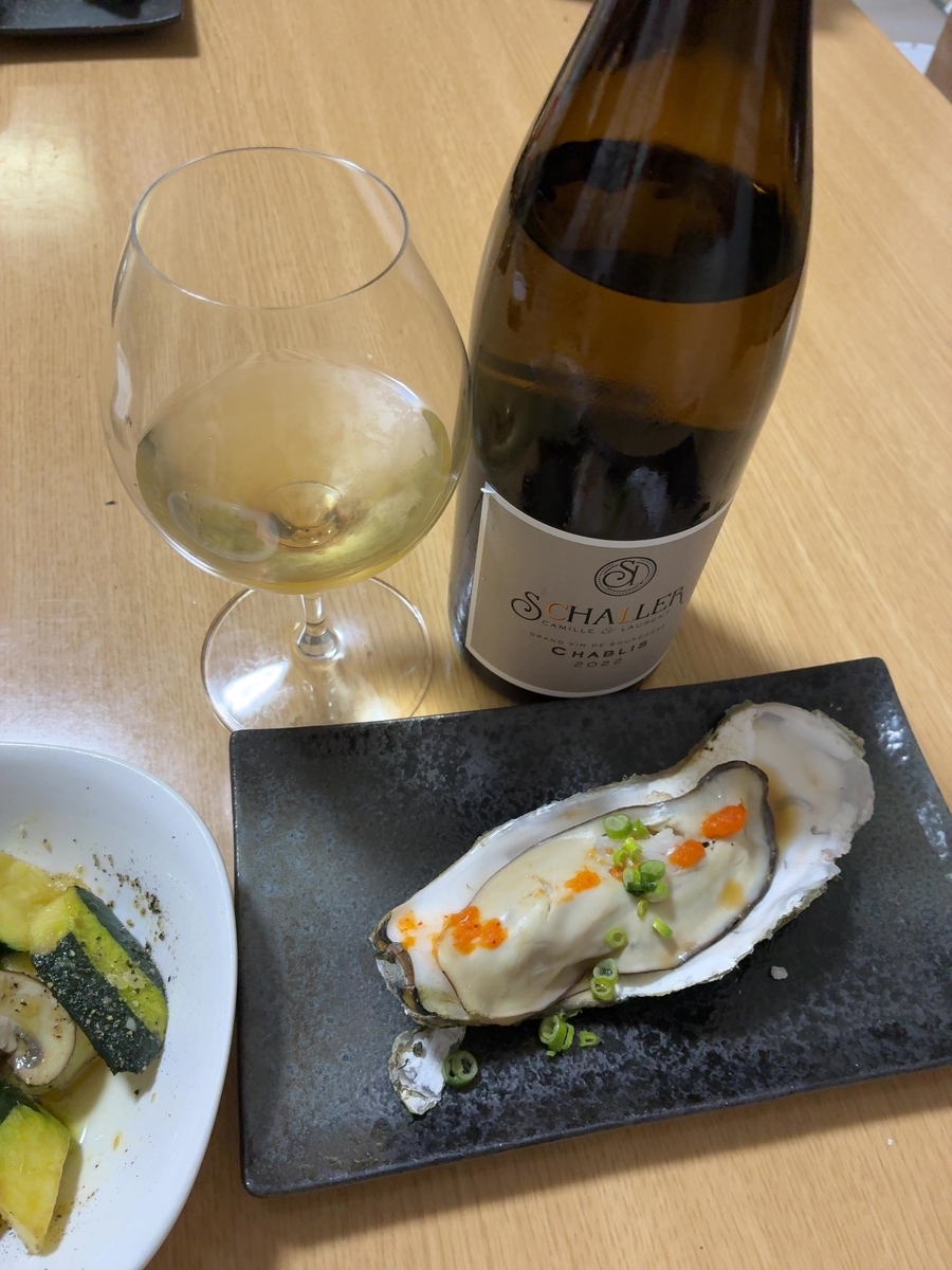 ワインと牡蠣、そして野菜の料理が写っています。 ワインボトルには「SCHALLER CHABLIS 2022」と書かれています。ワイングラスには白ワインが入っており、牡蠣はレモンとネギが添えられています。左側にはズッキーニとマッシュルームの料理が見えます。