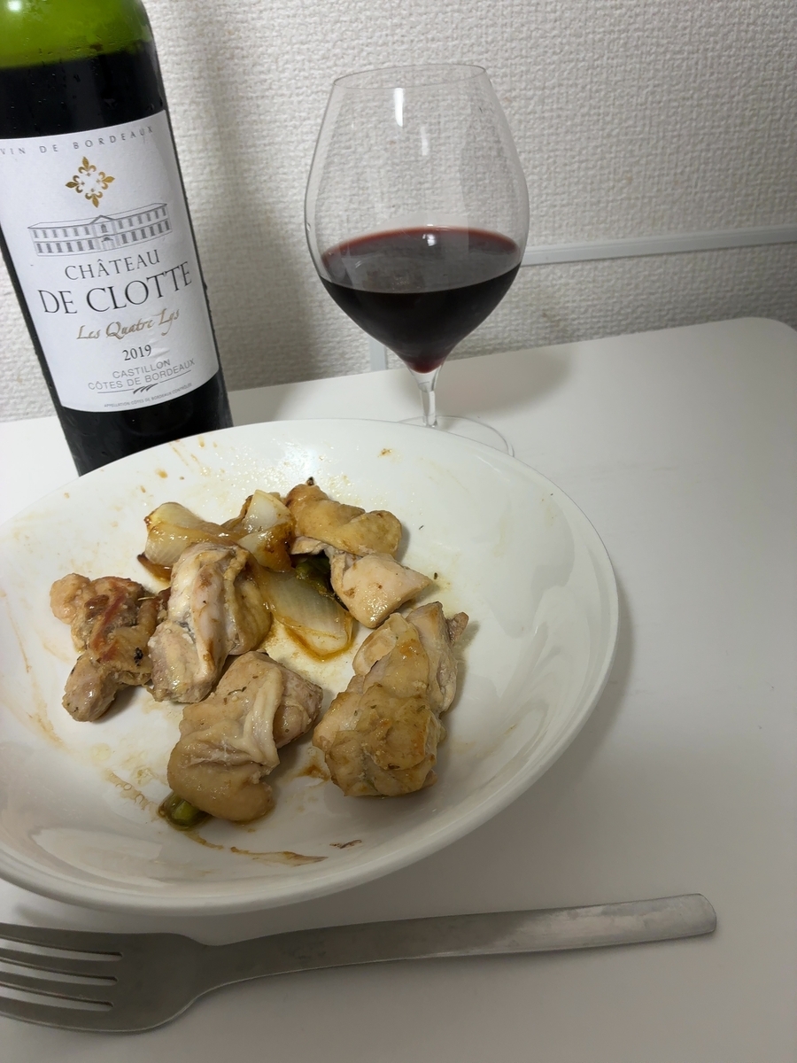 白いテーブルの上に白い深皿が置かれ、鶏もも肉のスパイスマリネ焼きが盛り付けられている。奥左にシャトー・ド・クロットのボトル、奥右にボルドーグラスに注がれた深いルビー色の赤ワイン。手前右にフォーク。