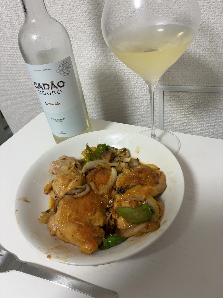 白いテーブルの上を俯瞰気味に撮影した2日目の晩酌の一場面。手前の白い丸皿に、バター・醤油・みりんで仕上げた鶏もも肉が複数の切り身に分かれて盛られており、照りのある濃い茶色のソースが絡んでいる。玉ねぎ・ピーマンが添えられ、香ばしそうな仕上がりに見える。奥には1日目と同じCADÃO DOUROのボトルと大ぶりのブルゴーニュグラスが並んでいる。右下にフォークが写っている。