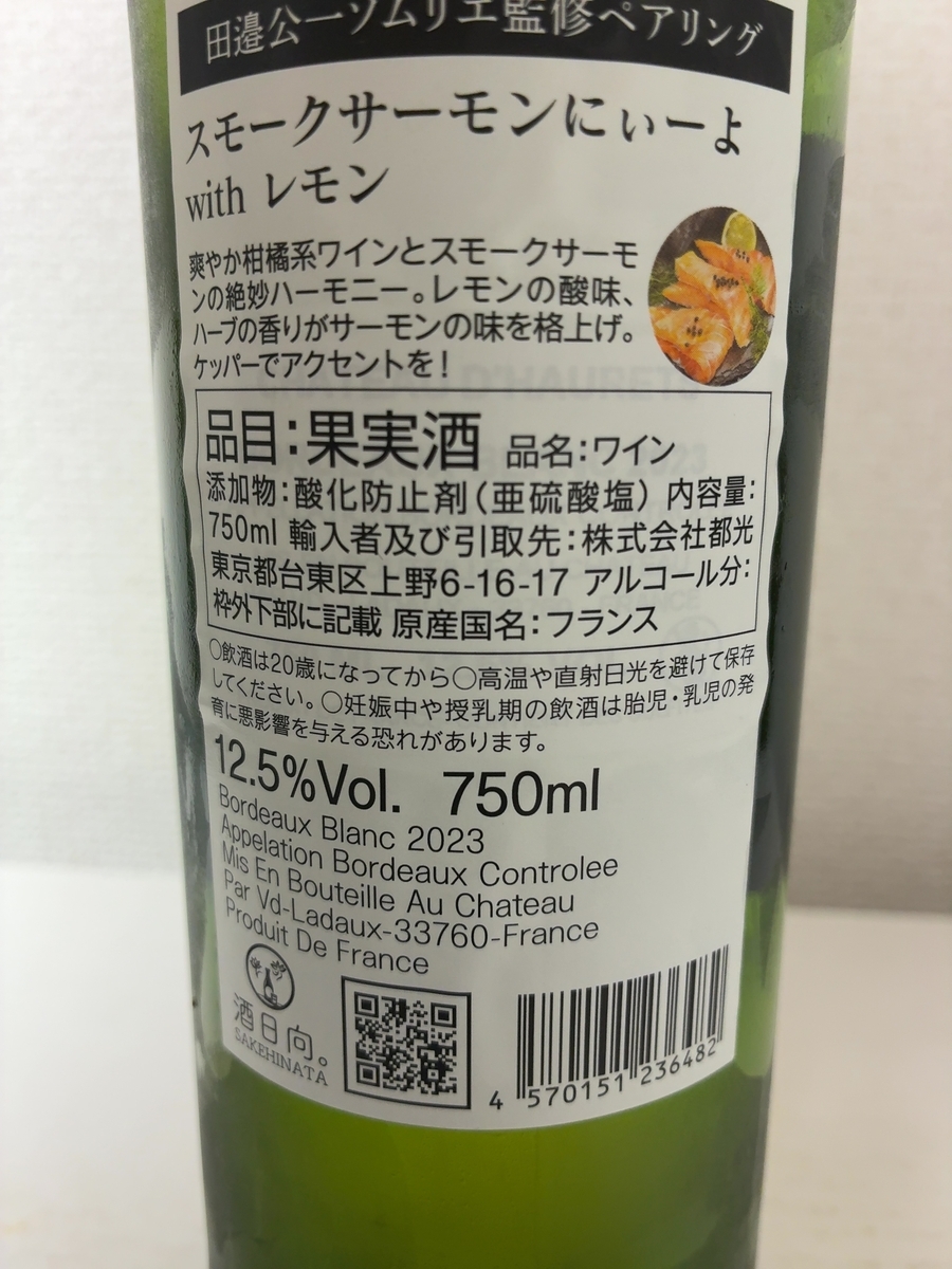 緑色のワインボトルの正面ラベル。黒いスレート板に盛られたオレンジ色のスモークサーモンとレモン、ディル、黒胡椒のイラストが黒地に描かれ、下部に白文字で「スモークサーモンにぃーよ with レモン」とある。