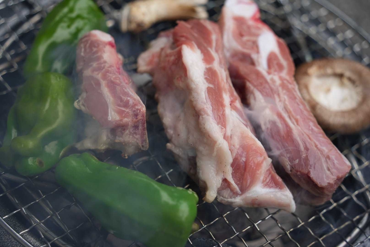 炭火グリルで焼かれる豚スペアリブとピーマン、しいたけの接写—立ちのぼる煙と焼き色がわかる