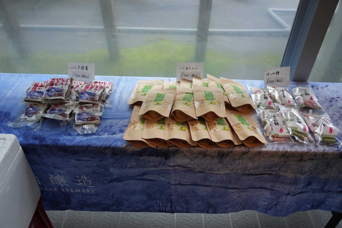 直売所の陳列台に並ぶ新規3品：いぶし大根漬・つぶならコーン・はっか糖（価格表示あり）