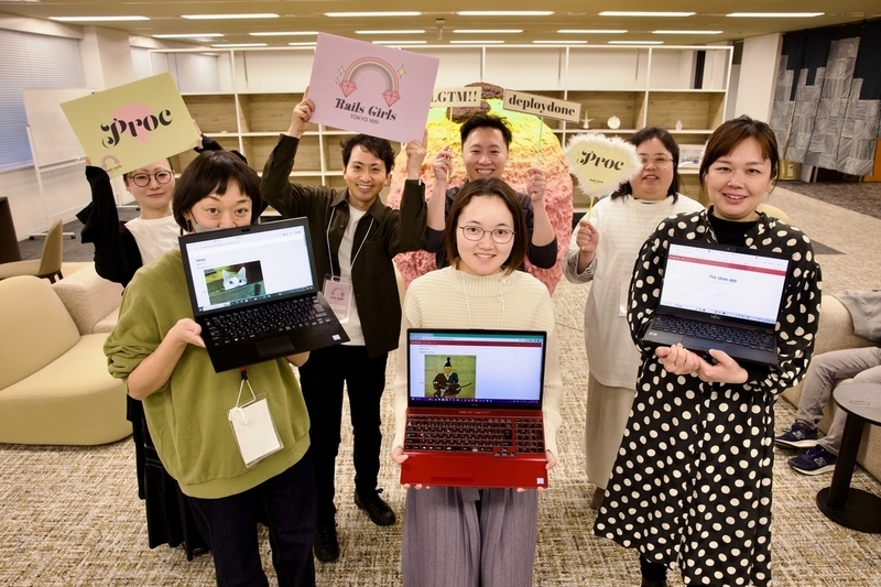Procチームの集合写真。7人の男女。前列の3名の女性は作ったアプリをラップトップで表示してこちらに見せている。やったー