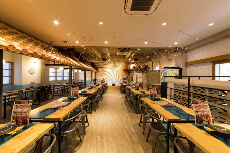 ご飯屋さんの写真。4人掛けの机が3列、大量に並んでいる。天井には、沖縄の漆喰を模した屋根がある