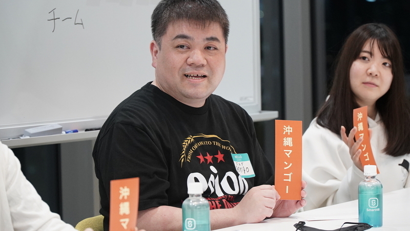 マンゴーの札を持って語るgongoさん。手前と奥にもマンゴーの札が並んでおり、計3名がマンゴーを選んでいることがわかる。