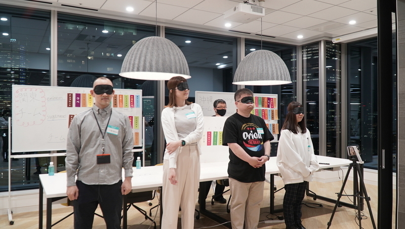 手前に並ぶ4名の挑戦者。全員アイマスクをつけている。その背後に正解の札が貼られているホワイトボードが持ち込まれる