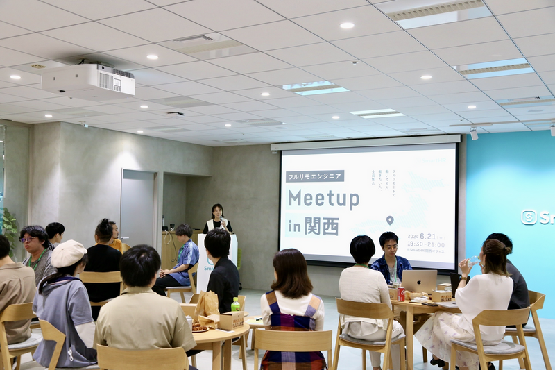 イベント開催中の写真。前方スクリーンに「フルリモエンジニアMeetup in 関西」の文字。演台に女性（futabaさん）が立って話している。