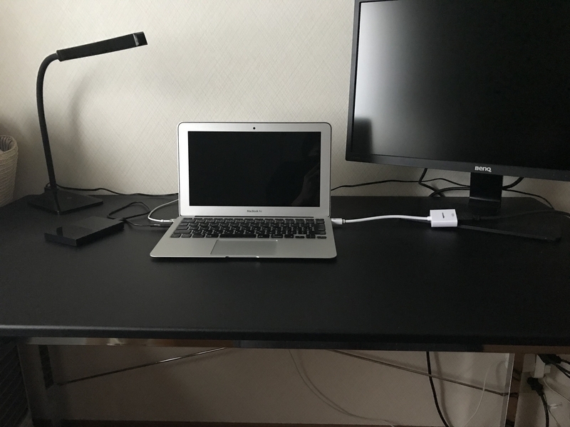 黒い机にMacのノートPMCとモニターと証明が置かれている。その他のものは見当たらずとてもシンプルなデスク環境。