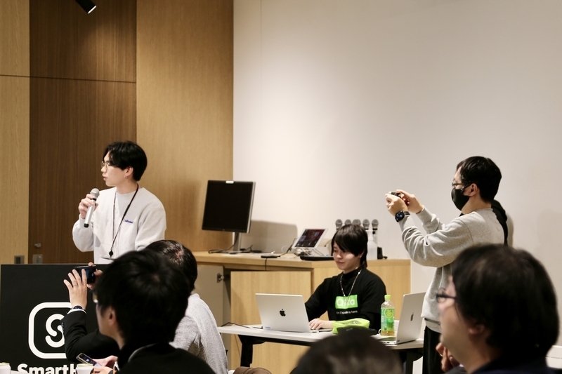 登壇するyamakeeeeeeeeenさん、yamakeeeeeeeeenさんを撮影するDevRel inaoさん