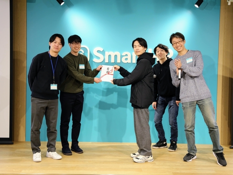 壇上で、優勝したチームに審査員がのし袋を渡している