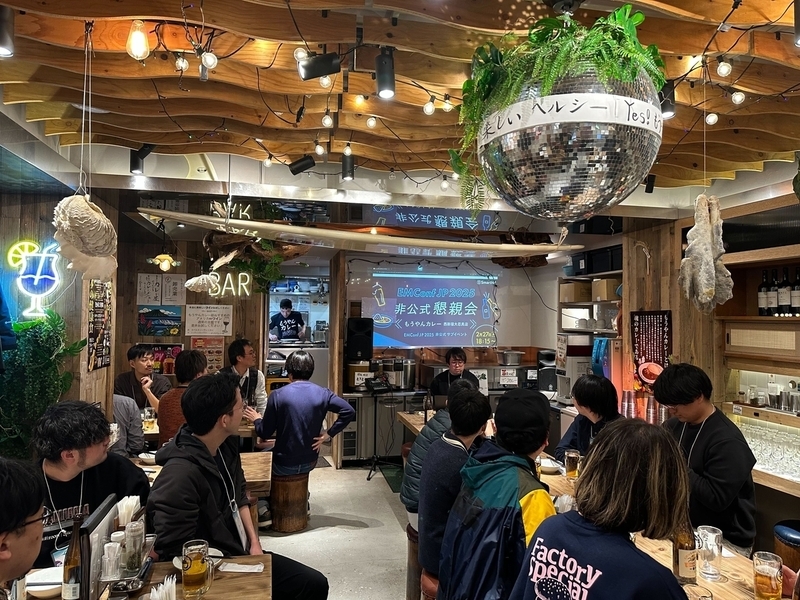 EMConfJP 2025非公式懇親会の会場写真。参加者が着席しスライド資料を見ている店内の様子