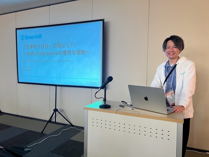 大きなモニターの横で、笑顔で写っている