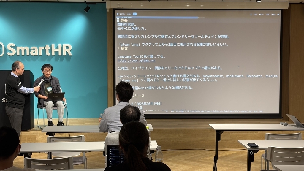 パソコンを膝に置いて壇上に座っており、Magnolia.Kさんがマイクを持っている
