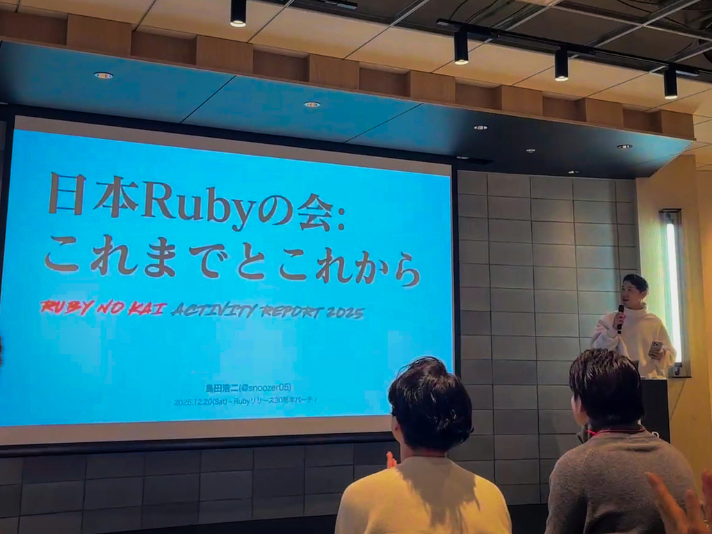 大きなスクリーンの隣で登壇されているしまださん