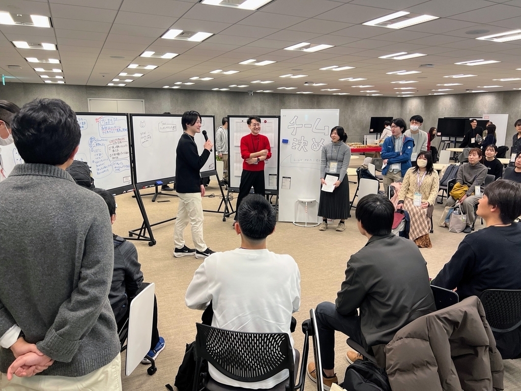 車座の参加者に向かって、マイクを持った人が書きたいテーマを発表している