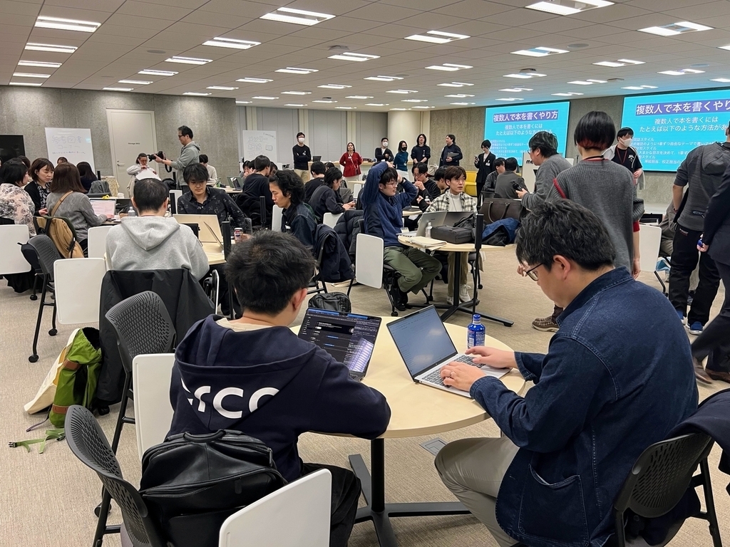 チームごとにテーブルに分かれて座り、画面に向かって作業をしている
