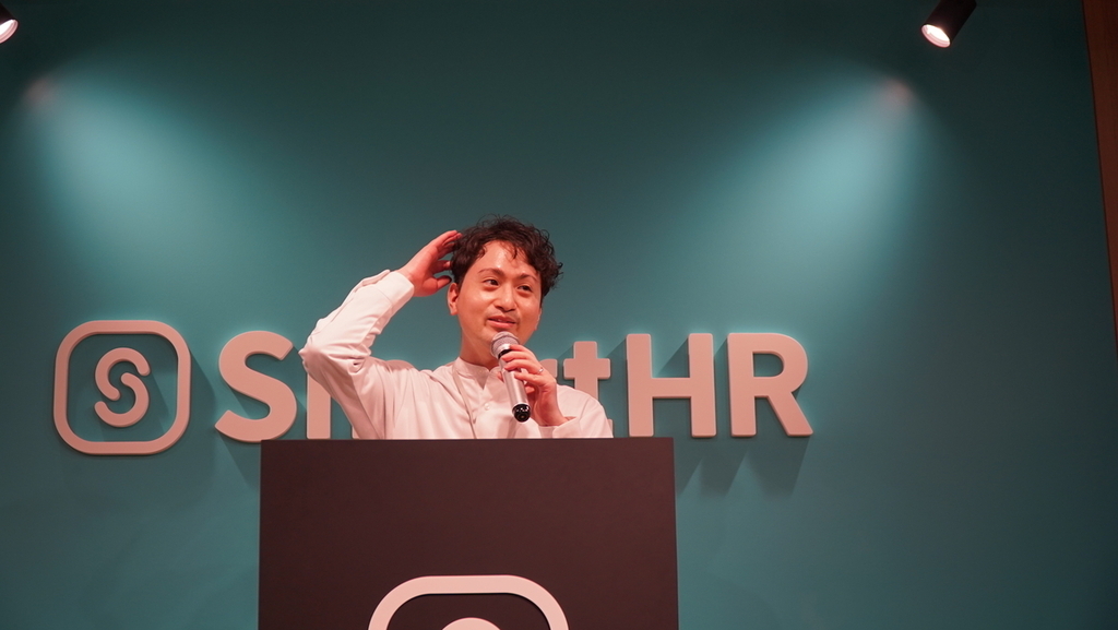 SmartHRのロゴの前でマイクを持ち話す男性の写真
