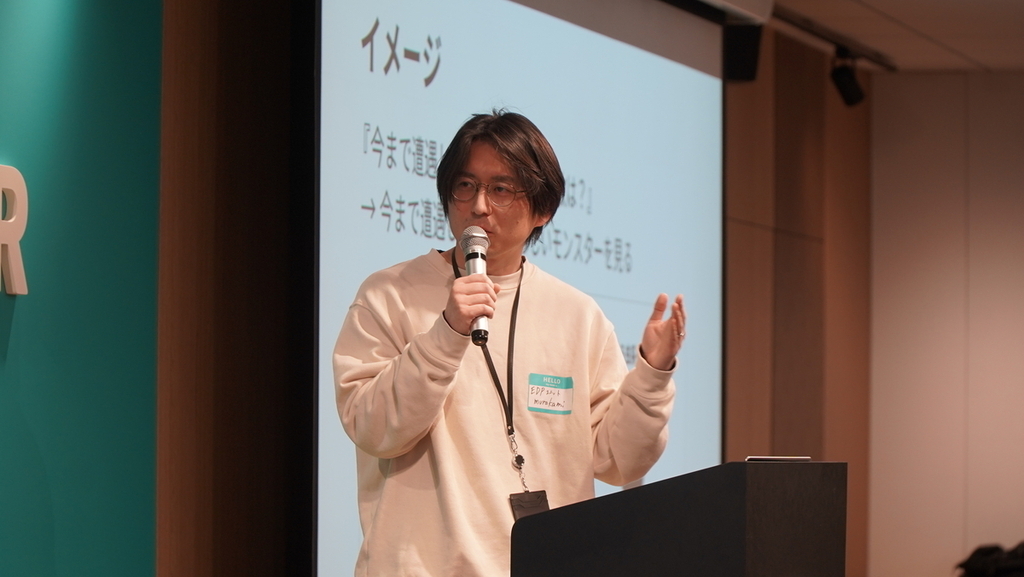 マイクを片手に持ち手を広げて語る男性の写真