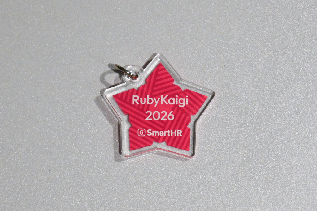 RubyKaigi 2026会場限定アクキーの実物。赤い縞模様の五稜郭の形に RubyKaigi 2026とSmartHRのロゴが入っている