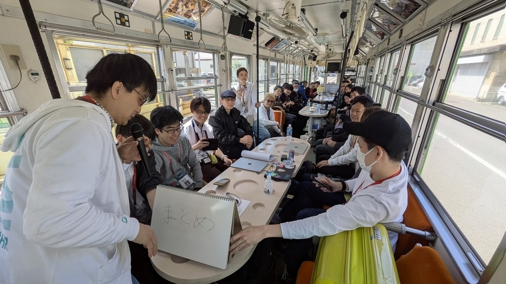 走行中の函館市電の車内で資料を手にLTを行うudzuraさん