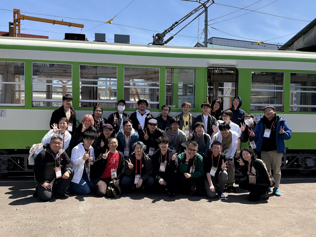 函館市電の車両を背景に参加者全員でポーズをとっている集合写真
