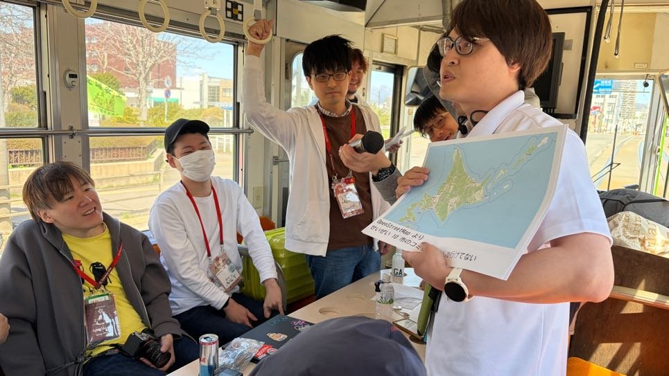 紙の資料を手にめくりながら車内で発表している登壇者