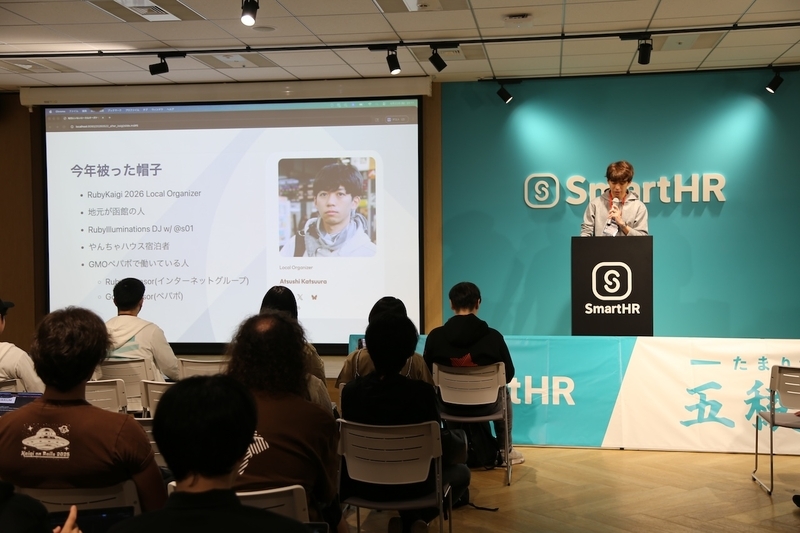 「今年被った帽子」という活動内容が書かれたスライドを背に、黒い演台からローカルオーガナイザーの泥臭い舞台裏を明かすikarugaさん