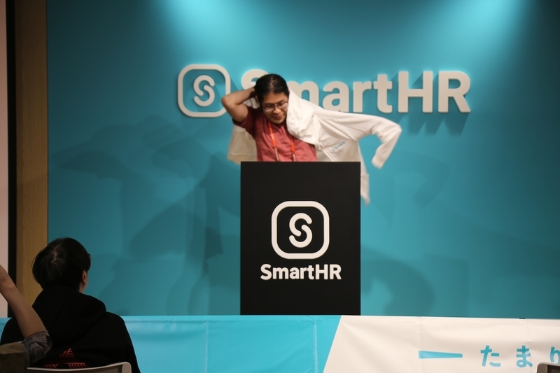 LTの最中にステージ上で、持参した白いSmartHRパーカーをサプライズで勢いよく羽織って着替えている、躍動感のあるYuichiro Kanekoさん