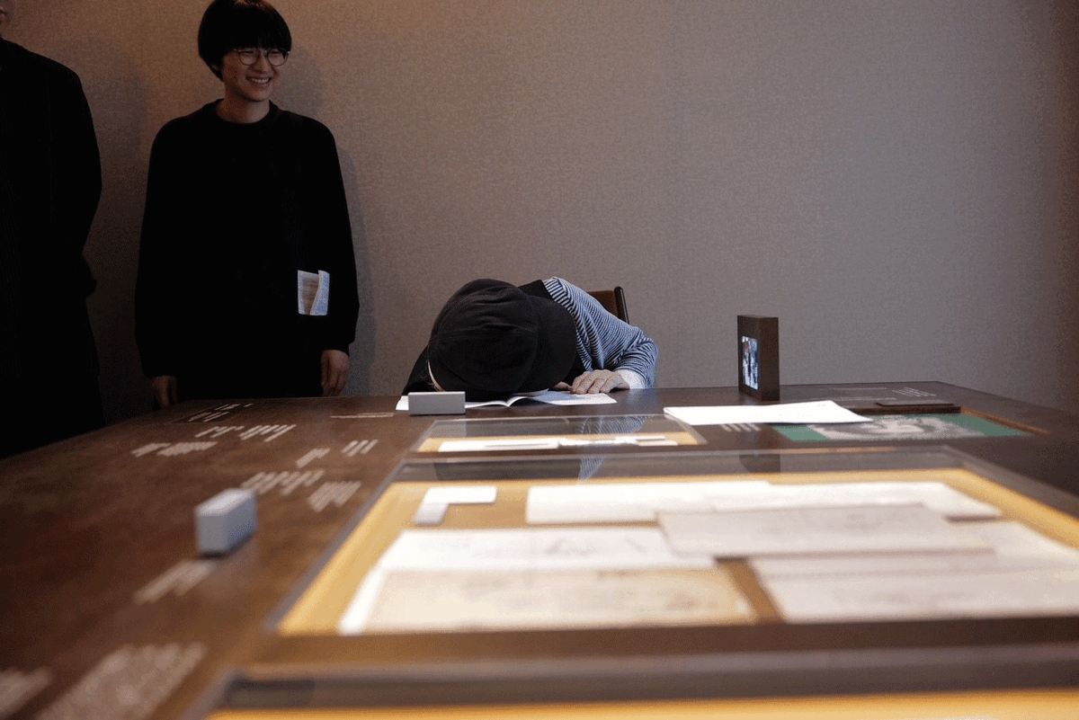 テーブルに耳を当てる細野。左は企画編集・デザインを行った三澤遥