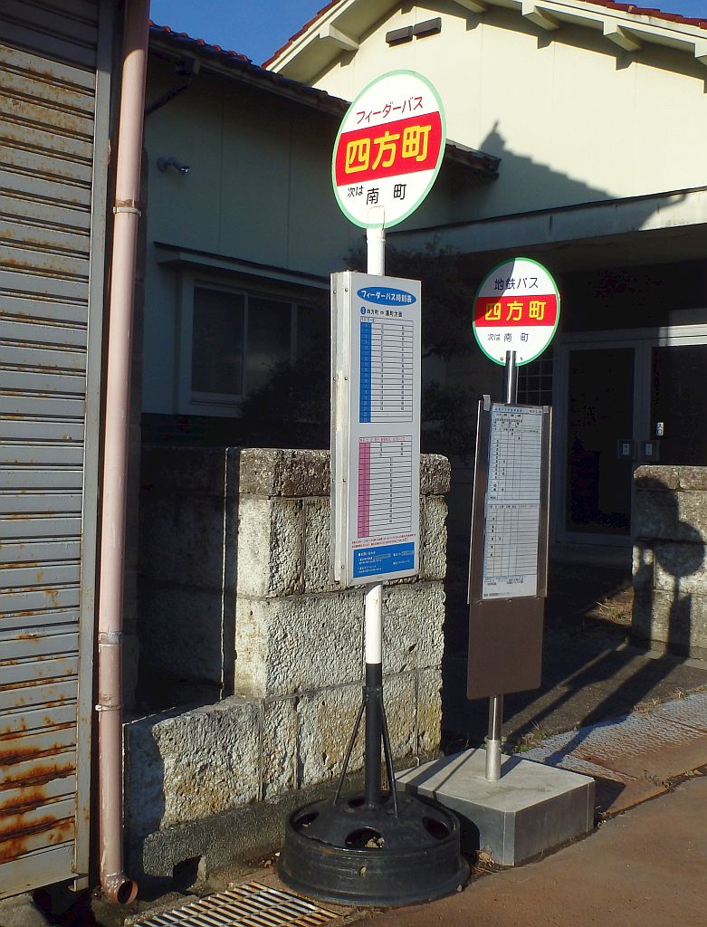 土台はタイヤのホイールで背の高い旧タイプバス停と、四角い型にコンクリートが詰まった土台から生えた背の低い新タイプバス停の比較