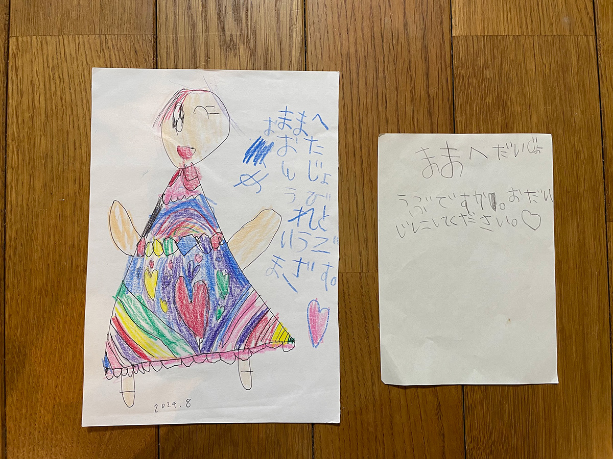 著者が娘からもらったお手紙が2枚並んでいる。左は誕生日にもらった手紙でカラフルなドレスに身を包んだ女性の絵が描いてある。右は著者が体調を崩して寝ていた時にもらったもので、子どもの字で「おだいじにしてください」などと書かれている