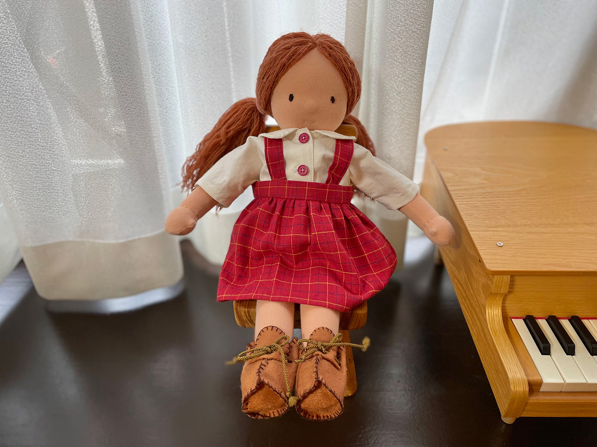 おばあちゃんが手作りしてくれたお人形の「みよちゃん」。2つ結びの髪型に、ブラウスと赤い吊りスカートを着ている