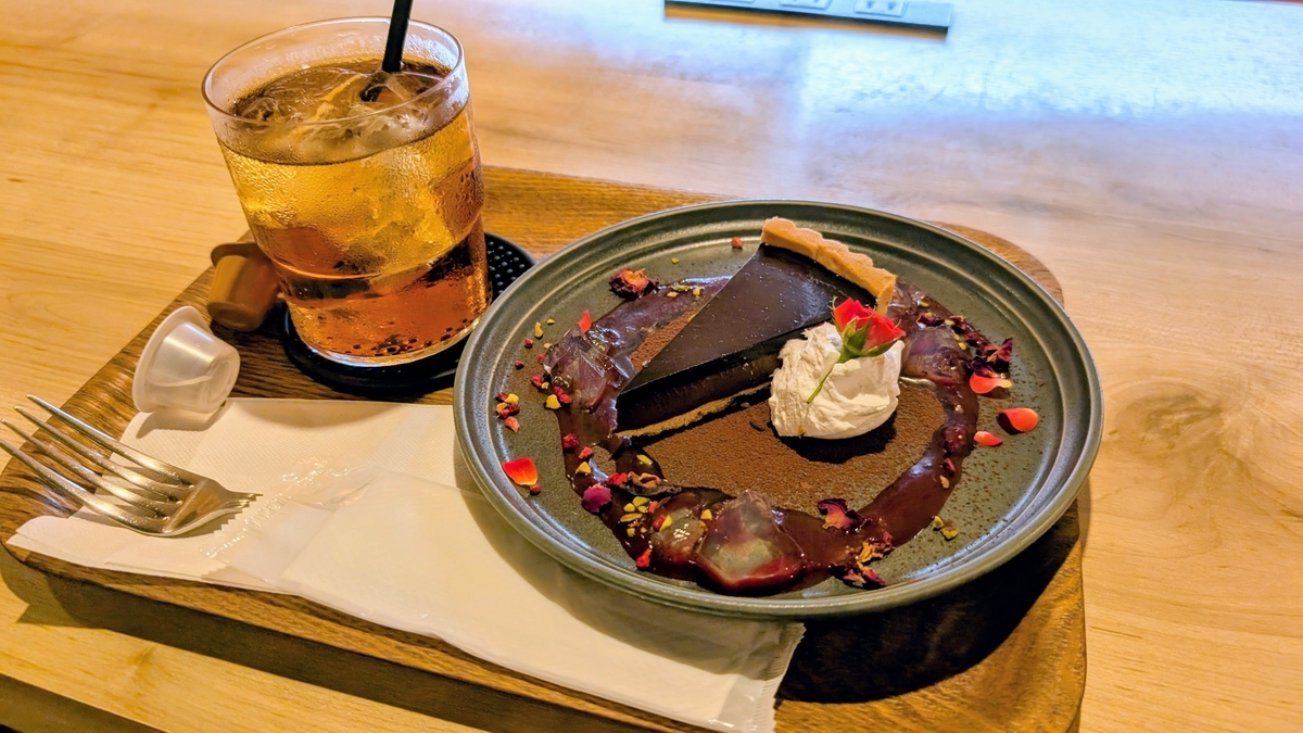 左側にアイスティー、右側にチョコレートタルト、ホイップクリームと小さなバラ、チョコレートソースを添えて