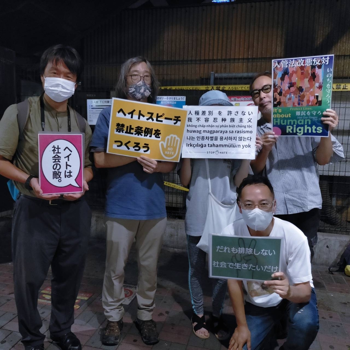 プラカードを持つ５人の人びとの写真。プラカードは「ヘイトは社会の敵」「ヘイトスピーチ禁止条例をつくろう」「人種差別を許さない」「入管法改悪反対」「誰も排除しない　社会で生きたいだけ」という内容。