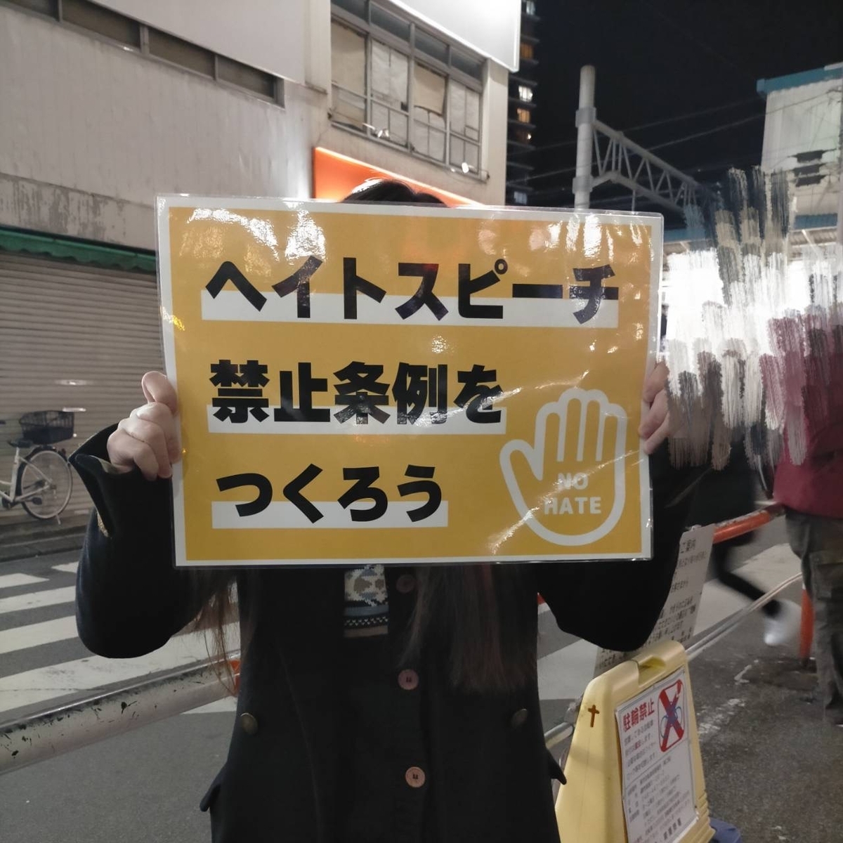 プラカードを持つ人の写真。「ヘイトスピーチ禁止条例をつくろう」と書かれている。