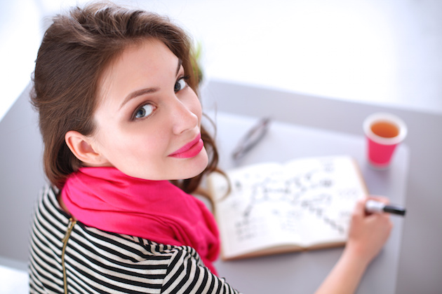 Young woman writes to diary on a white table