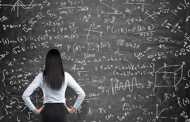 Rear view of a thoughtful woman who tries to solve math problems. Math calculations on black chalk board.
