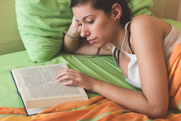 Young Woman Reading a Book on the Bed
