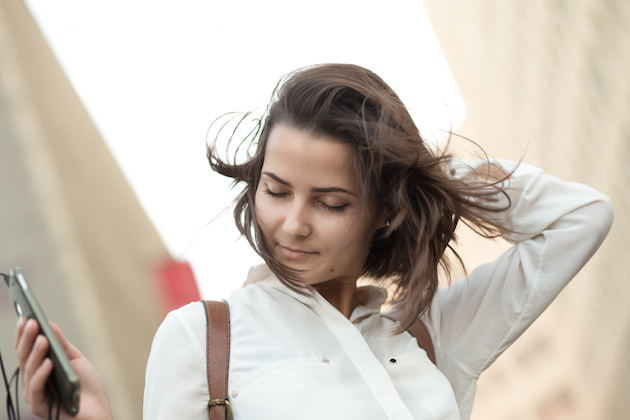 Pretty girl walking in city with phone. Hair fly.