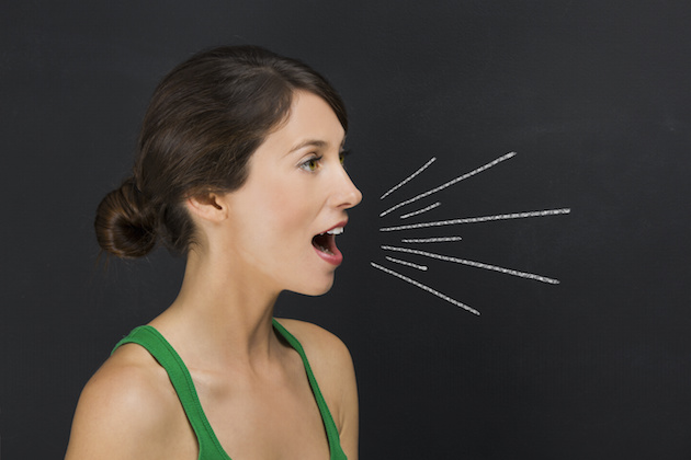 Beautiful young student giving a speech over a chalkboard with rays coming out from her mouth