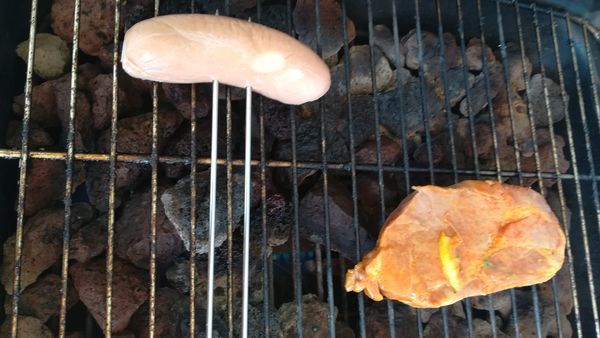 バーベキューのコンロの上の鉄板の右手に肉、左手には串２本を刺したセルブラが焼かれている。
