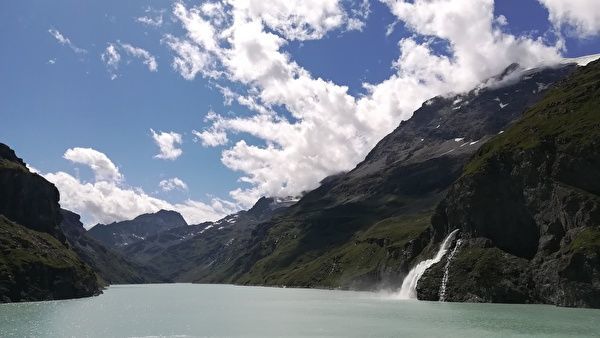 ダムの湖に山から水が流れ込んでいる。青空と白い雲を背景に山と湖が映えている。