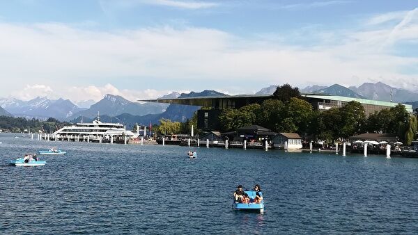 ルツェルンの湖の景色。ボートを楽しむ人々や遊覧船。遠景には雪をかぶったスイスの山なみ。